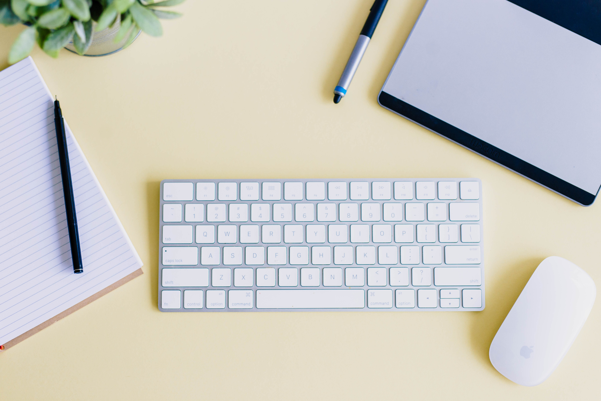 A wireless keyboard and mouse next to some note books and pens.